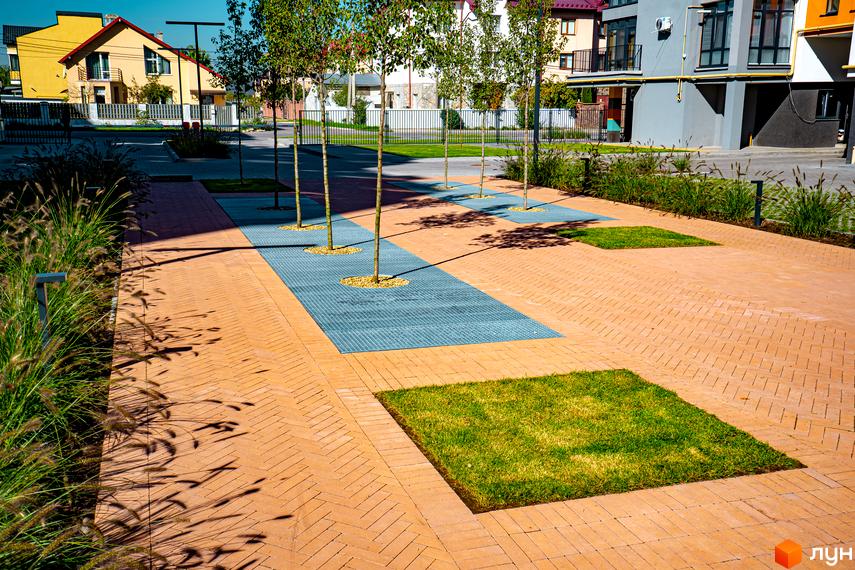 Житловий комплекс Квартал Краківський. Територія з бруківкою, газонами та деревами. Будинки з сірими та жовтими фасадами.