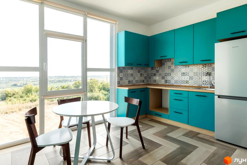 Інтер'єр кухні в Житловому комплексі Арден Курортний з бірюзовими шафами та обіднім столом біля великого вікна.