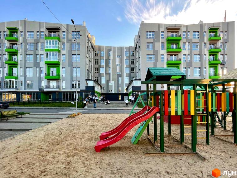 Житловий комплекс ЕкоПарк з яскравими зеленими балконами та дитячим майданчиком з гірками та різнокольоровими елементами. Сучасна архітектура та облаштована прибудинкова територія.