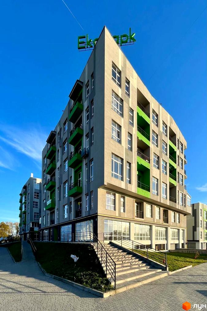 Зовнішній вигляд житлового комплексу ЕкоПарк з сірими фасадами та зеленими балконами. Поруч розташована прибудинкова територія з доріжками та сходами.
