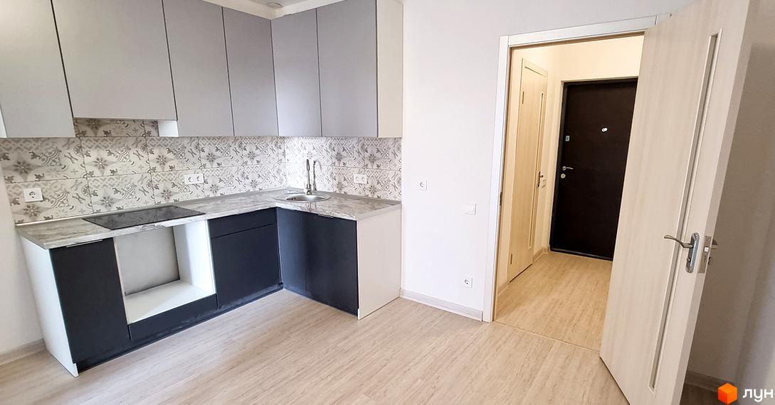 Сучасна кухня з сірими фасадами та плиткою з візерунком. Поруч двері, що ведуть до коридору з іншими дверима.