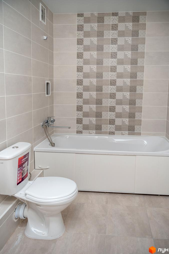 Ванна кімната в Житловому містечку ARTVILLE з білим унітазом, ванною та стінами, облицьованими світлою плиткою з декоративним візерунком.