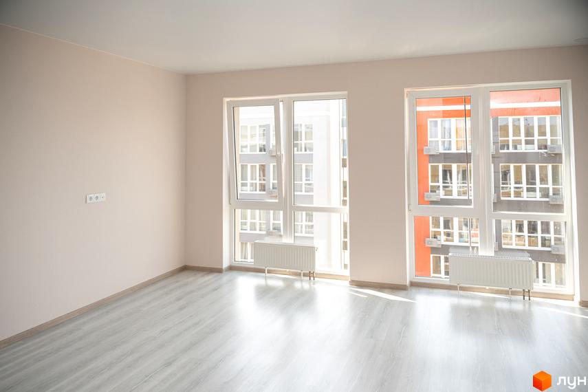 Житлове містечко ARTVILLE. Фото порожньої кімнати з великими вікнами, з яких видно фасади сусідніх будівель.