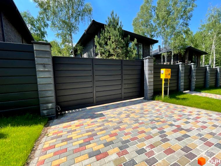 Будинки Котеджного містечка Elegant House з темними фасадами та дахами. Перед ними чорні ворота, паркан та кольорова бруківка на проїзді.