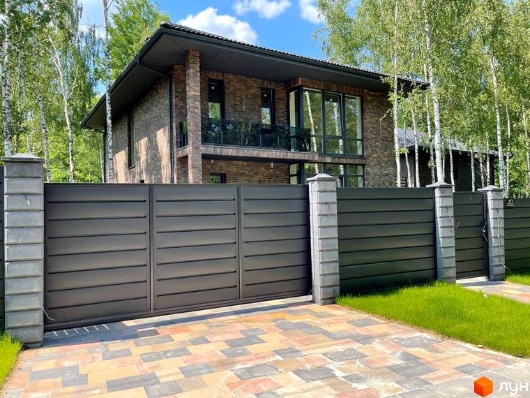 Фасад будинку з коричневої цегли та темна огорожа Котеджного містечка Elegant House. На подвір'ї укладена бруківка.