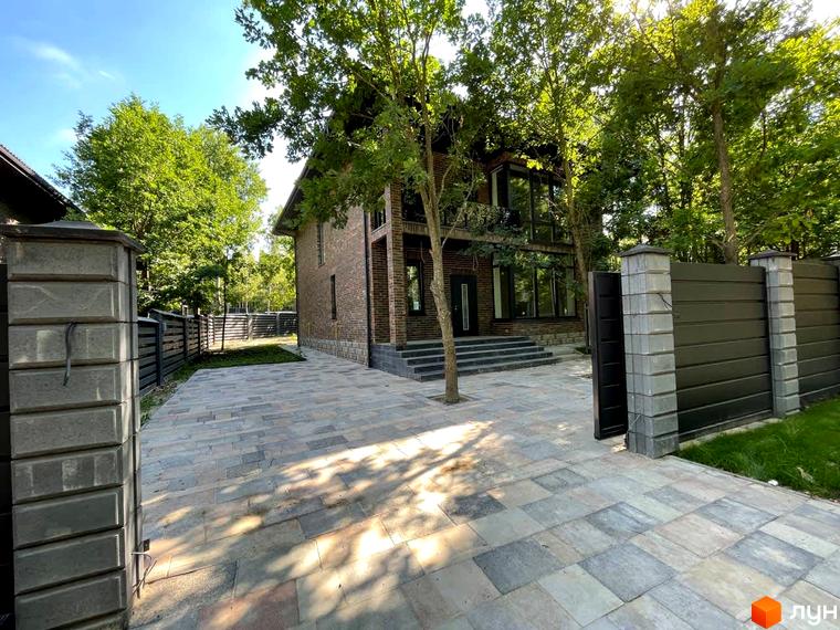 Будинок Котеджного містечка Elegant House з цегляними стінами, великими вікнами та сходами. Прибудинкова територія вимощена бруківкою, є огорожа.