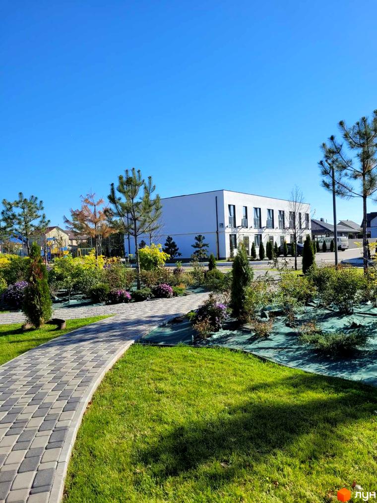 Будинок DREAM HOUSE з панорамними вікнами та зеленою прибудинковою територією з доріжками та деревами.