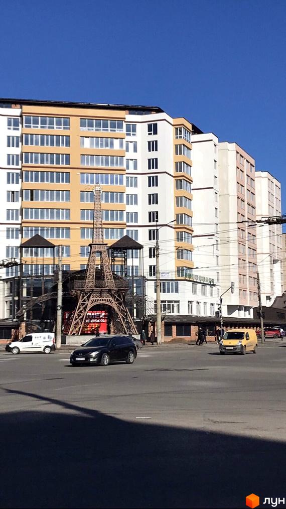 Житловий комплекс Комфорт представлений багатоповерховими будинками з білими та помаранчевими фасадами. Перед комплексом розташована вулиця з автомобілями та декоративна скульптура Ейфелевої вежі.