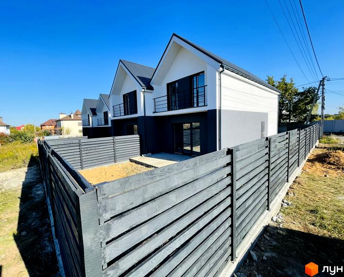 Дуплекси „На Зоряному“: двоповерхові будинки з чорними дахами та балконами, огороджені дерев'яною огорожею. Навколо будівельний майданчик.