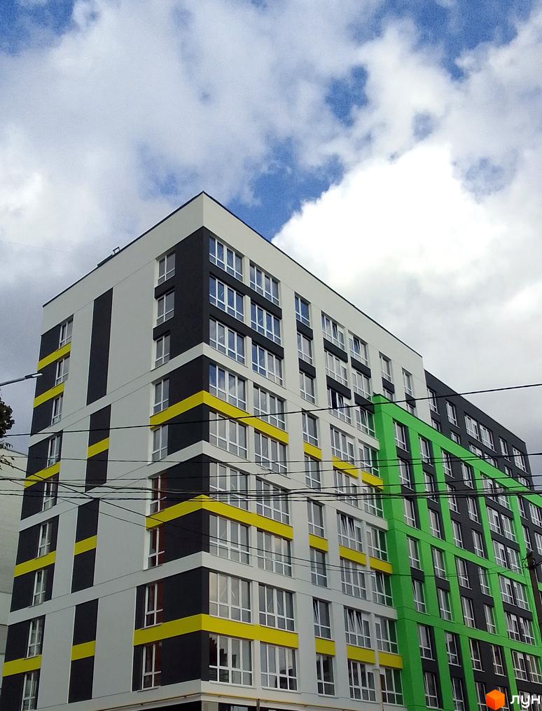 Фасад житлового комплексу на вул. Заміська, 16, з білими, сірими та яскраво-жовтими елементами, а також зеленою секцією. Багато вікон, хмарне небо.