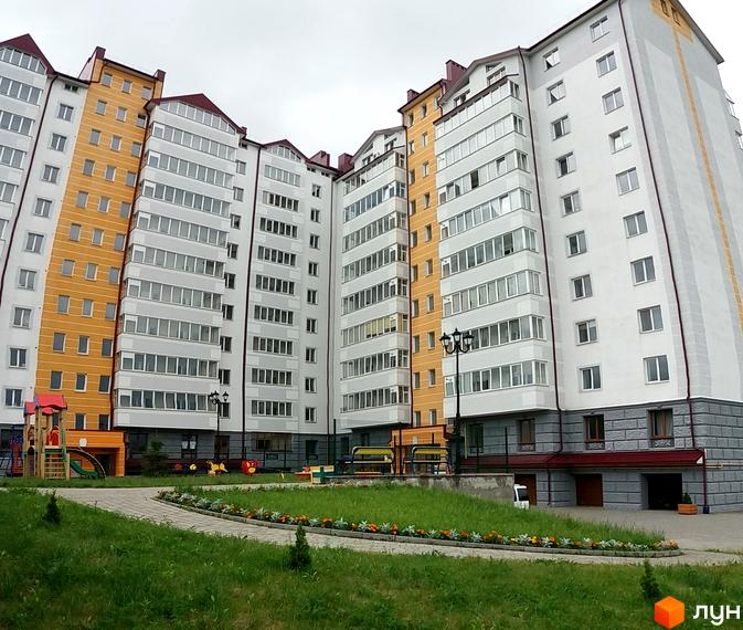 Зовнішній вигляд новобудови ЖК Ювілейний: багатоповерховий будинок з жовтими та білими фасадами, заскленими балконами. Прибудинкова територія з дитячим майданчиком та зеленими насадженнями.