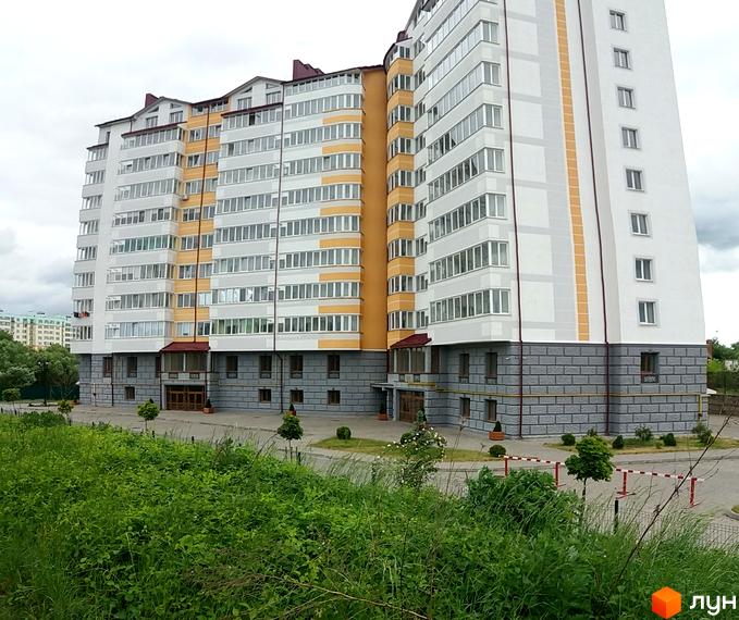 Житловий комплекс Ювілейний. Зовнішній вигляд новобудови з жовтими та білими елементами фасаду, сірою цегляною обробкою цоколя та прибудинковою територією з зеленню.