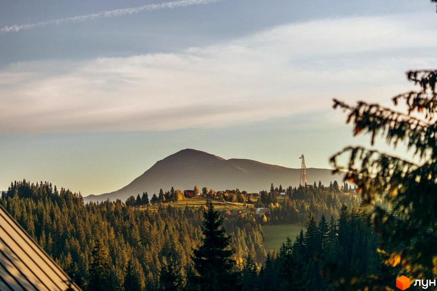 Фото Котеджного містечка SKOGUR на фоні гір та лісу. Вигляд на дахи будинків, зелені дерева та пагорби.