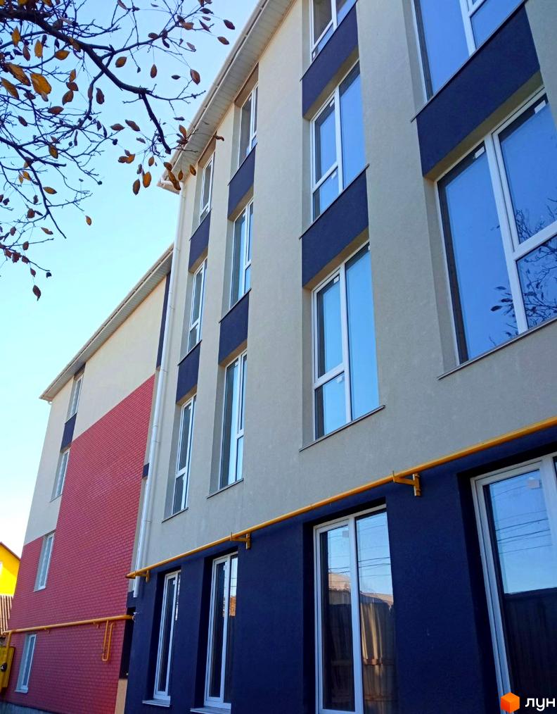 Фасад житлового комплексу Брусника з цегляною та штукатурною обробкою, вікнами та газовою трубою.