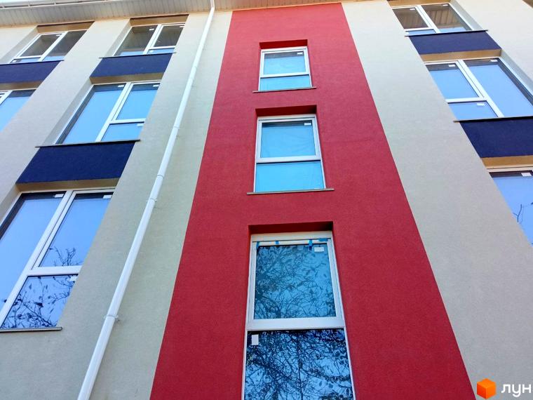 Фасад житлового комплексу Брусника з вікнами та червоно-бежевими елементами. Зовнішній вигляд новобудови з великими вікнами.