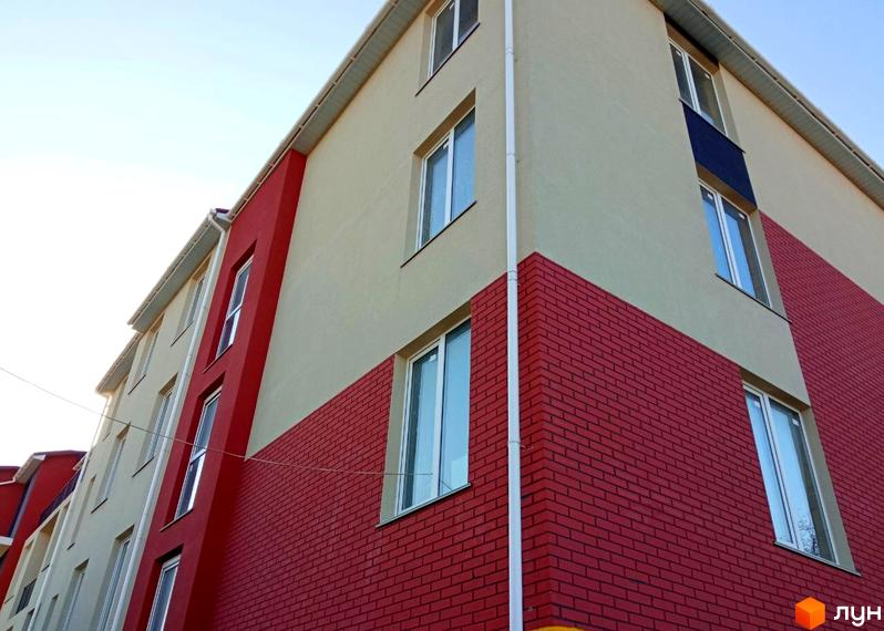 Зовнішній вигляд новобудови ЖК Брусника з червоною цегляною обробкою нижнього поверху та бежевими стінами верхніх поверхів.