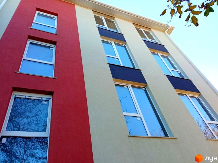 Фасад житлового комплексу Брусника з червоними та бежевими елементами та великими вікнами. Зовнішній вигляд новобудови.