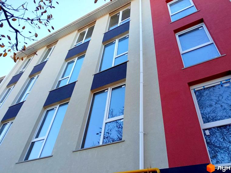 Будинок житлового комплексу Брусника з червоно-бежевим фасадом та великими вікнами. Зовнішній вигляд новобудови.