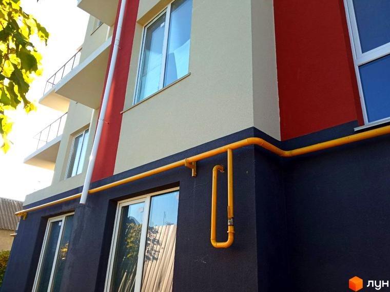 Зовнішній вигляд новобудови ЖК Брусника з балконами та вікнами. Зовнішні комунікації, такі як газові труби, проходять вздовж фасаду будівлі.