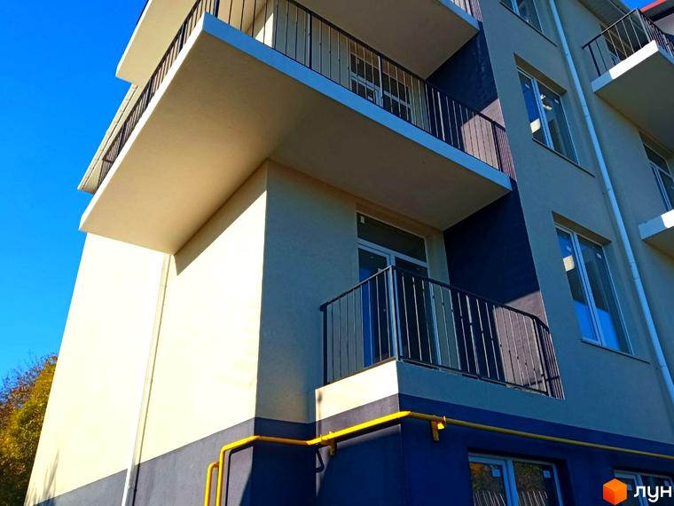 Зовнішній вигляд новобудови ЖК Брусника з балконами та вікнами на фоні блакитного неба. Будинок має світло-бежевий та темно-синій фасади.