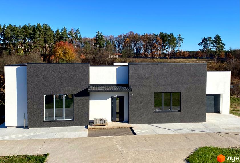 Сучасний двоповерховий будинок з білою та темно-сірою штукатуркою, великими вікнами та прибудинковою територією з деревами на фоні.