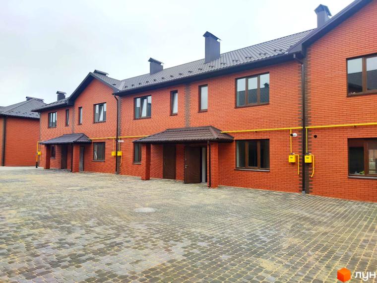 Котеджне містечко Екологічне: ряд двоповерхових будинків з червоної цегли та темними дахами. Перед будинками викладена бруківка.