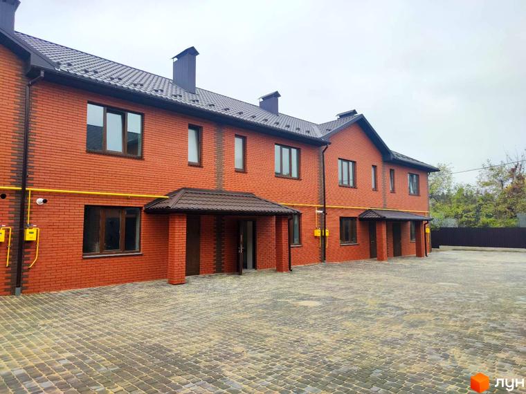 Зображення фасаду та прибудинкової території Котеджного містечка Екологічне. Двоповерхові будинки з червоної цегли та тротуарна плитка на подвір'ї.