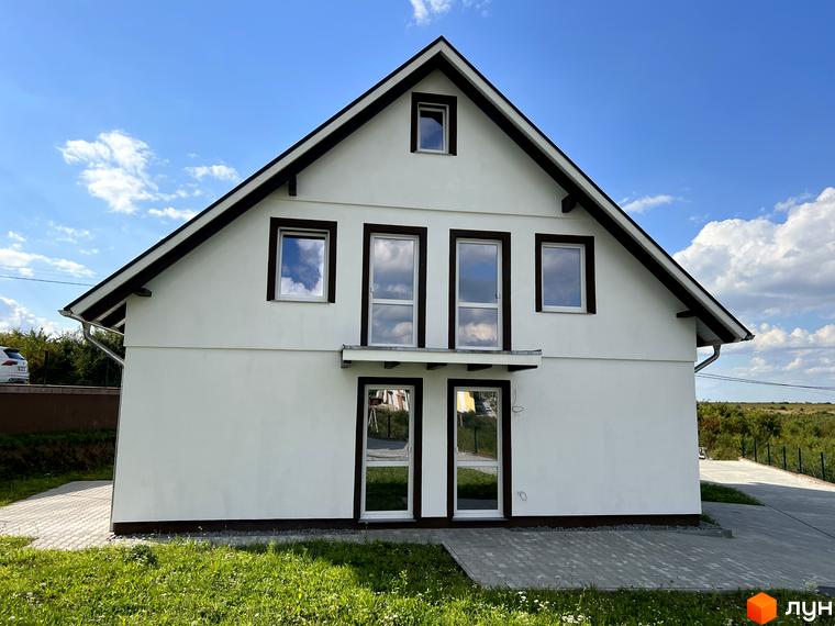 Зовнішній вигляд будинку в котеджному містечку КМ MEINDORF з великими вікнами та білою фасадною штукатуркою. Прибудинкова територія з бруківкою та зеленою травою.