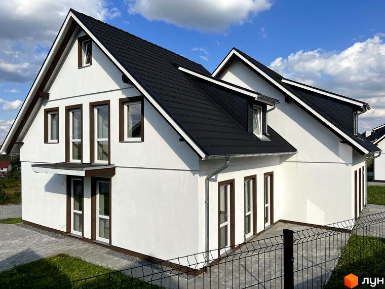 Котеджне містечко MEINDORF: білий двоповерховий будинок з чорним дахом та коричневими вікнами на тлі блакитного неба з хмарами. Поруч розташована прибудинкова територія з парканом та зеленою травою.