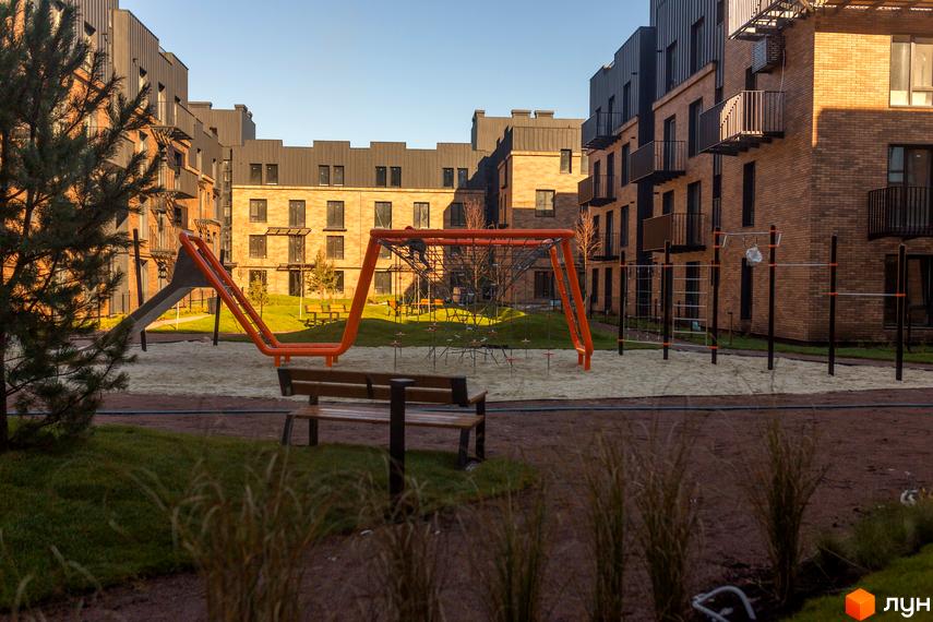 Житловий комплекс Клубне містечко 12 з цегляними фасадами та дитячим майданчиком. Сучасна архітектура та облаштована прибудинкова територія.