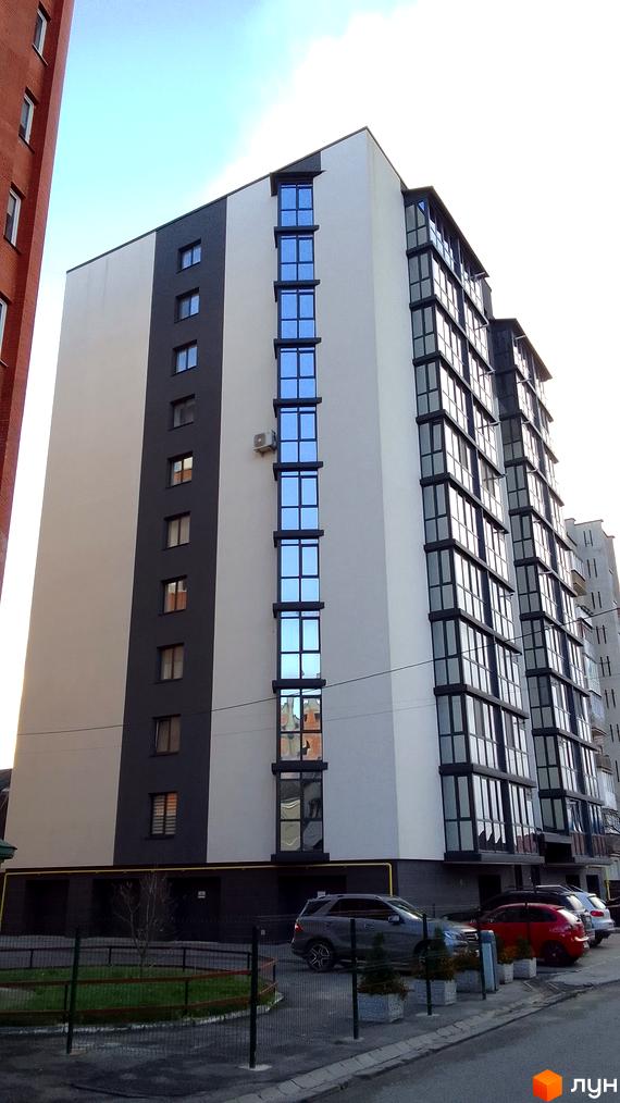 Зовнішній вигляд новобудови на вул. Данила Нечая, 6, з великими вікнами та сірими елементами фасаду. На прибудинковій території розташовані автомобілі та зелені насадження.