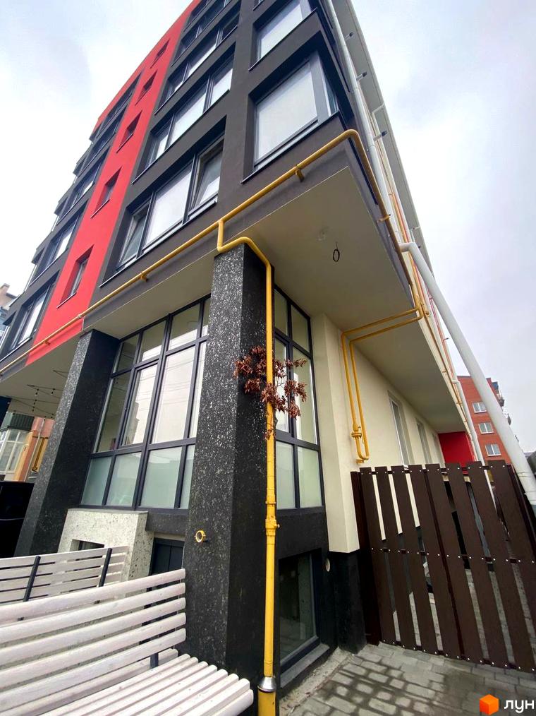 Зовнішній вигляд будинку в Житловому комплексі Central Avenue з червоними та сірими фасадами. На передньому плані лавка та елементи благоустрою.