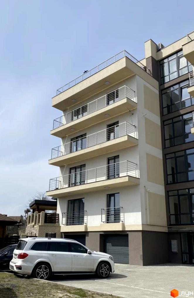 Зовнішній вигляд житлового комплексу Беладжіо з балконами та вікнами, прибудинкова територія з автомобілем.