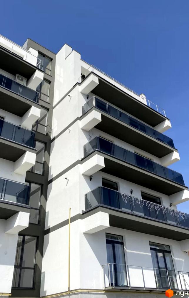 Фасад новобудови ЖК Беладжіо з балконами та скляними огорожами на фоні блакитного неба. Зовнішній вигляд будинку з сучасними архітектурними елементами.