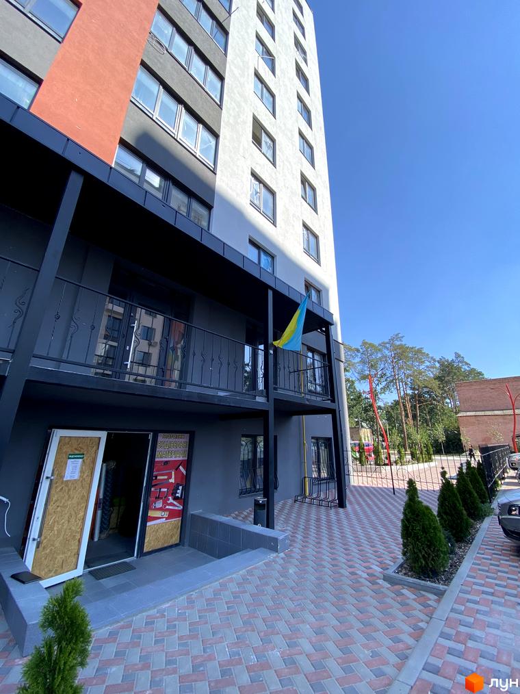 Зовнішній вигляд новобудови ЖК Green Life-3 з фасадом сірого та червоного кольору, балконами та прибудинковою територією з бруківки та зелених насаджень.