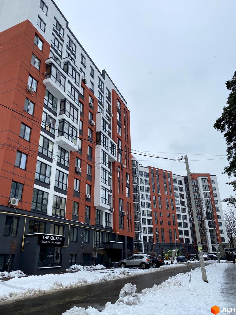 Житловий комплекс Green Life-3. Багатоповерхові будинки з червоно-білими фасадами та великими вікнами, розташовані біля дороги, засніжена прибудинкова територія.