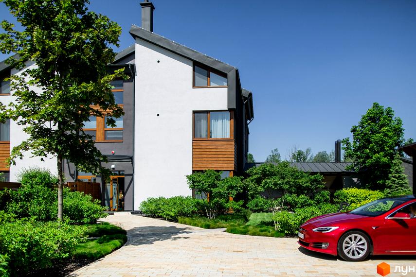 Зображення будинку з терасами. Фасад будинку пофарбований у білий та сірий кольори. На території є доглянутий газон та червоний електрокар Tesla.