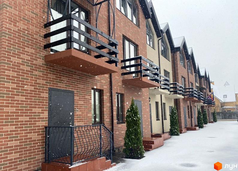 Цегляні таунхауси Modern House з балконами та чорними кованими поручнями. На вулиці сніг, перед будинками висаджені туї.