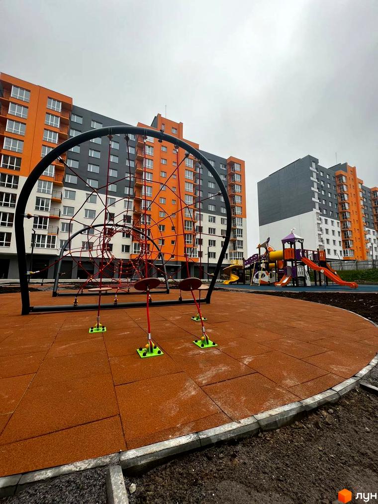 Житловий комплекс Сімейний COMFORT. Сучасний дитячий майданчик з яскравими гірками та мотузковим комплексом на тлі оранжево-сірих багатоповерхових будинків.