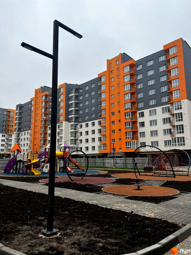 Житловий комплекс Сімейний COMFORT з помаранчевими та сірими фасадами. На прибудинковій території дитячий майданчик з різнокольоровими елементами.