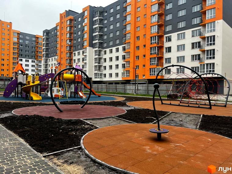 Житловий комплекс Сімейний COMFORT: сучасні будинки з яскравими фасадами та облаштований дитячий майданчик з різнокольоровими гірками та гойдалками.