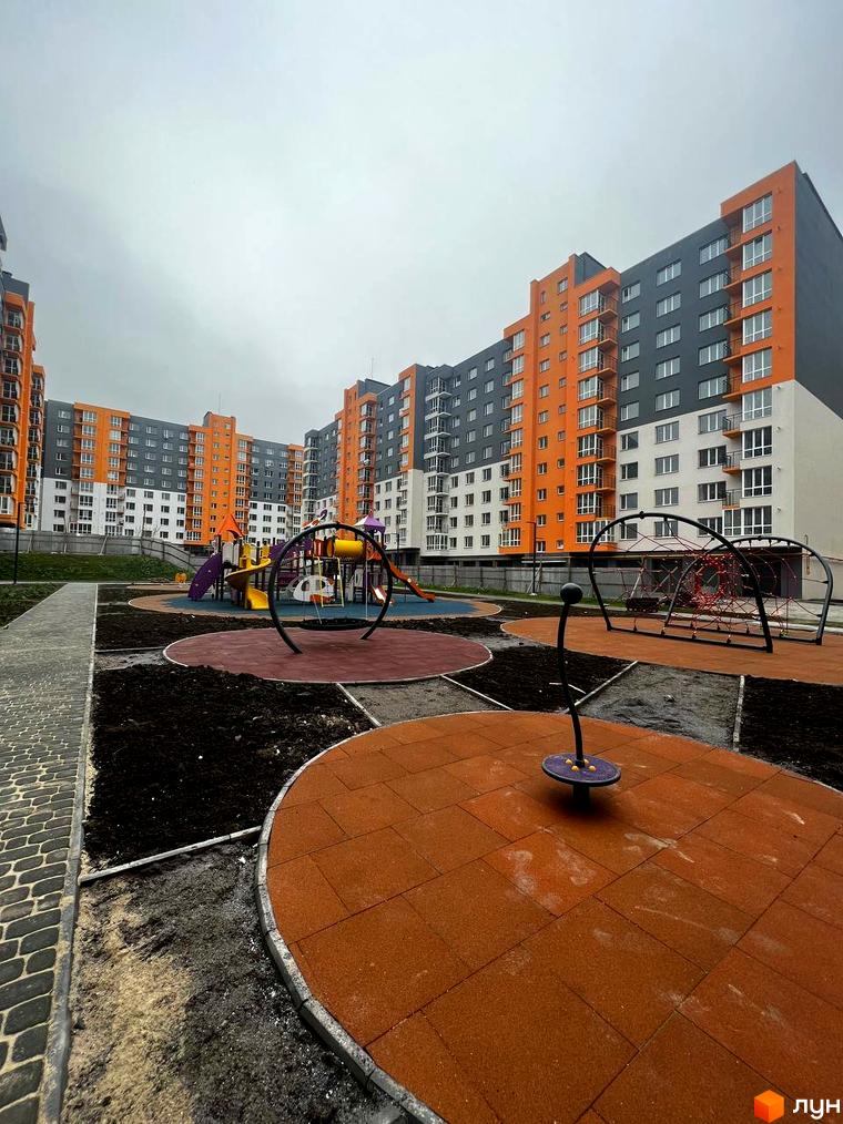 Житловий комплекс Сімейний COMFORT з оранжево-сірими фасадами та дитячим майданчиком з гумовим покриттям. Сучасний житловий комплекс з елементами благоустрою.