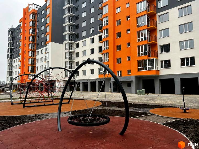 Житловий комплекс Сімейний COMFORT: яскрава новобудова з оранжевими та сірими фасадами, сучасний дитячий майданчик з гойдалками та сітками.