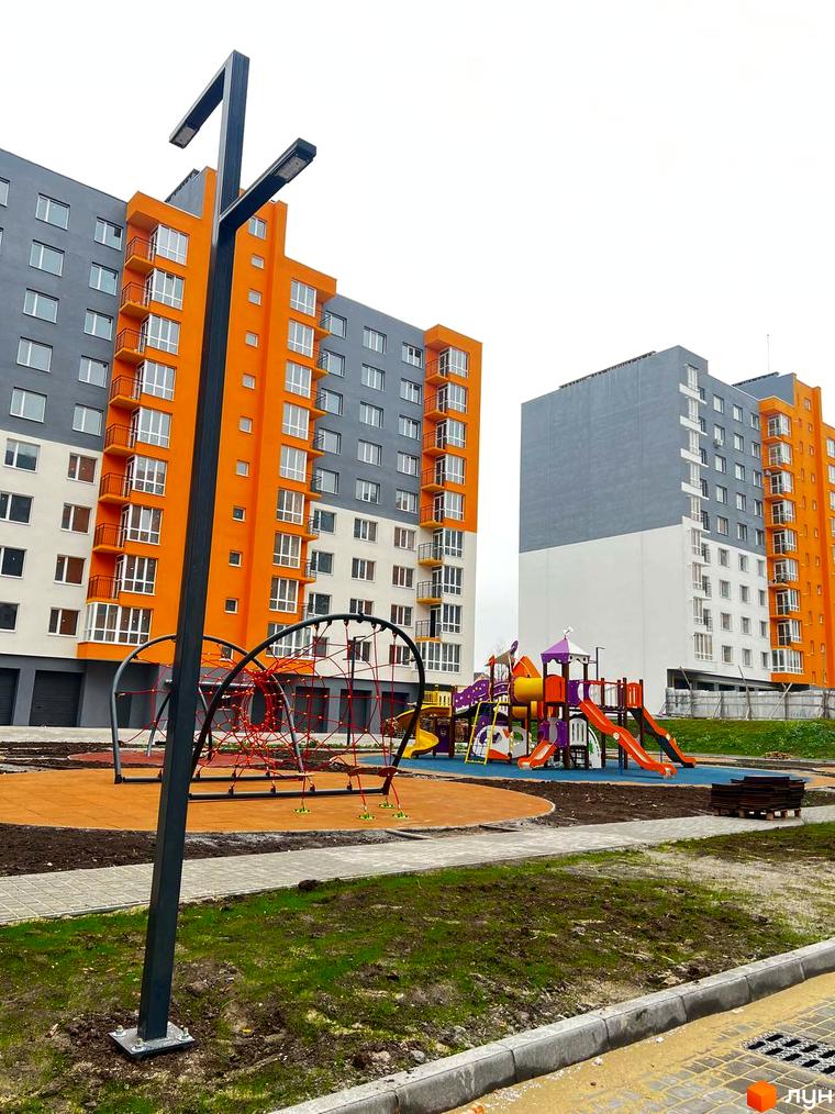 Житловий комплекс Сімейний COMFORT з яскравою оранжево-сірою фасадною частиною та сучасною дитячою зоною для ігор. На території новобудови розташовані яскраві гірки та ігрові конструкції.