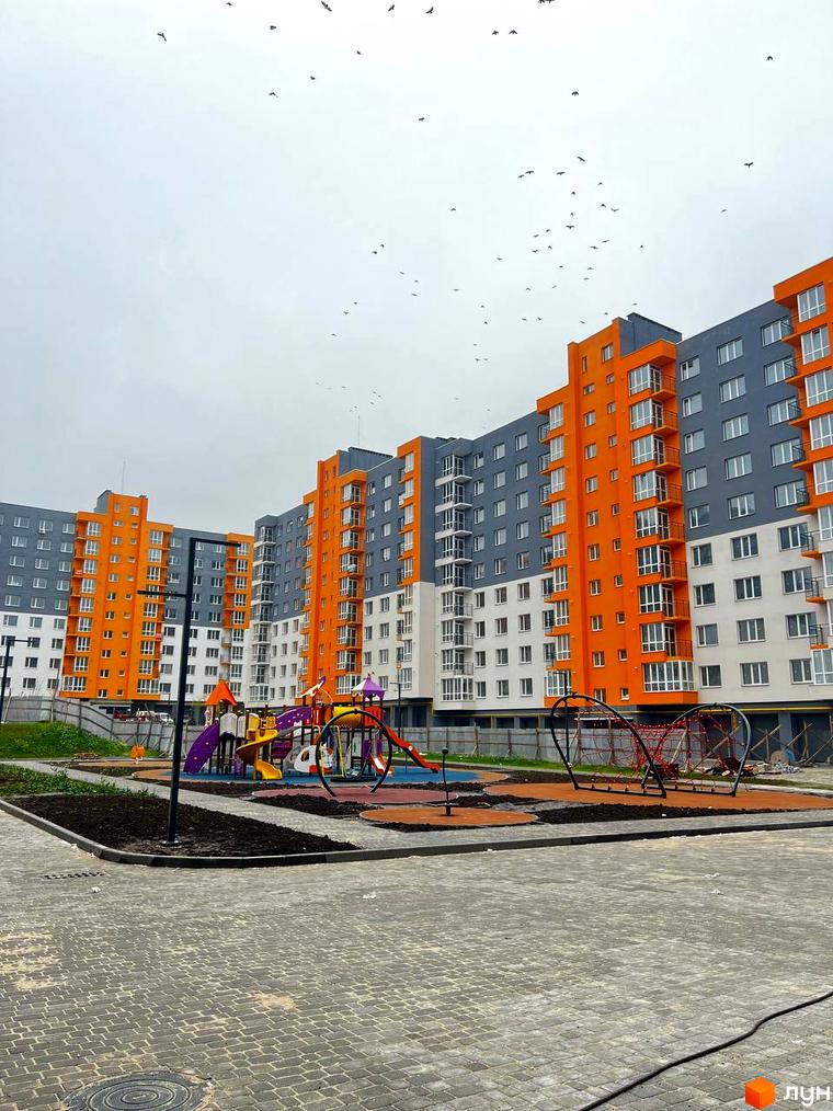 Новобудова ЖК Сімейний COMFORT з яскравими помаранчевими та сірими фасадами. На території облаштований дитячий майданчик із різнокольоровими гірками та безпечним покриттям.