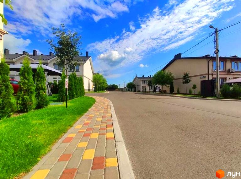 Котеджне містечко Паларіс: будинки світлих відтінків з темними дахами, доглянуті газони та кольорова бруківка на тротуарі.