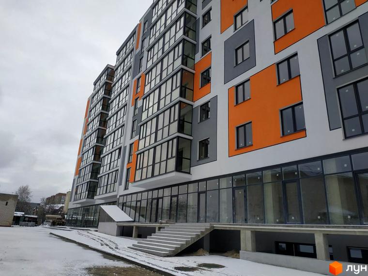 Зображення фасаду Житлового комплексу Orange City з білими, сірими та помаранчевими панелями, великими вікнами та засніженою прибудинковою територією.