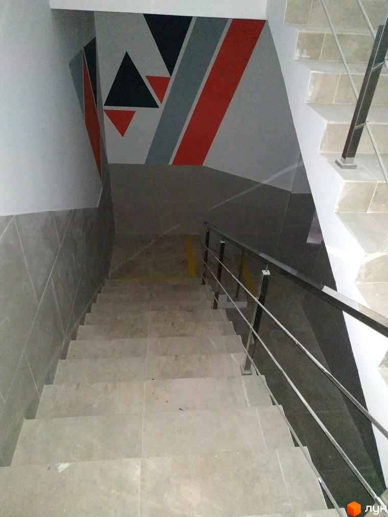 Сходовий простір Новобудови Orange City з металевими поручнями та стінами, оздобленими геометричними візерунками.