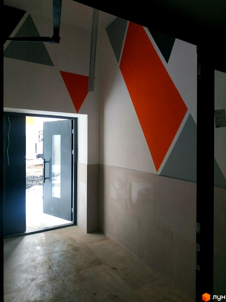 Вхідна група Новобудови Orange City з геометричним оздобленням стін. Вид на прибудинкову територію через відкриті двері.