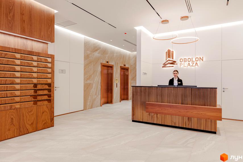 Стильний хол ЖК Obolon Plaza з ресепшн, ліфтами та поштовими скриньками. Сучасний дизайн інтер'єру з дерев'яними елементами та мармуровим оздобленням.